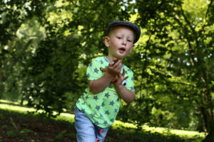 Malý kluk s dřevěnou hračkou na pozadí stromů