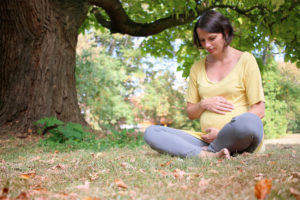 Těhotná žena sedící na zemi pod velkým stromem