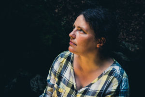 Portrét mladé ženy v kostkované košili v tmavém lese