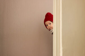 Little child`s head in a red cap peeks out between light-colored walls