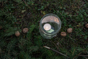 Burning candle in a glass jar on forest floor