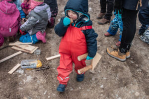 Little boy walks among people, eats bread and holds a part of wooden feeder