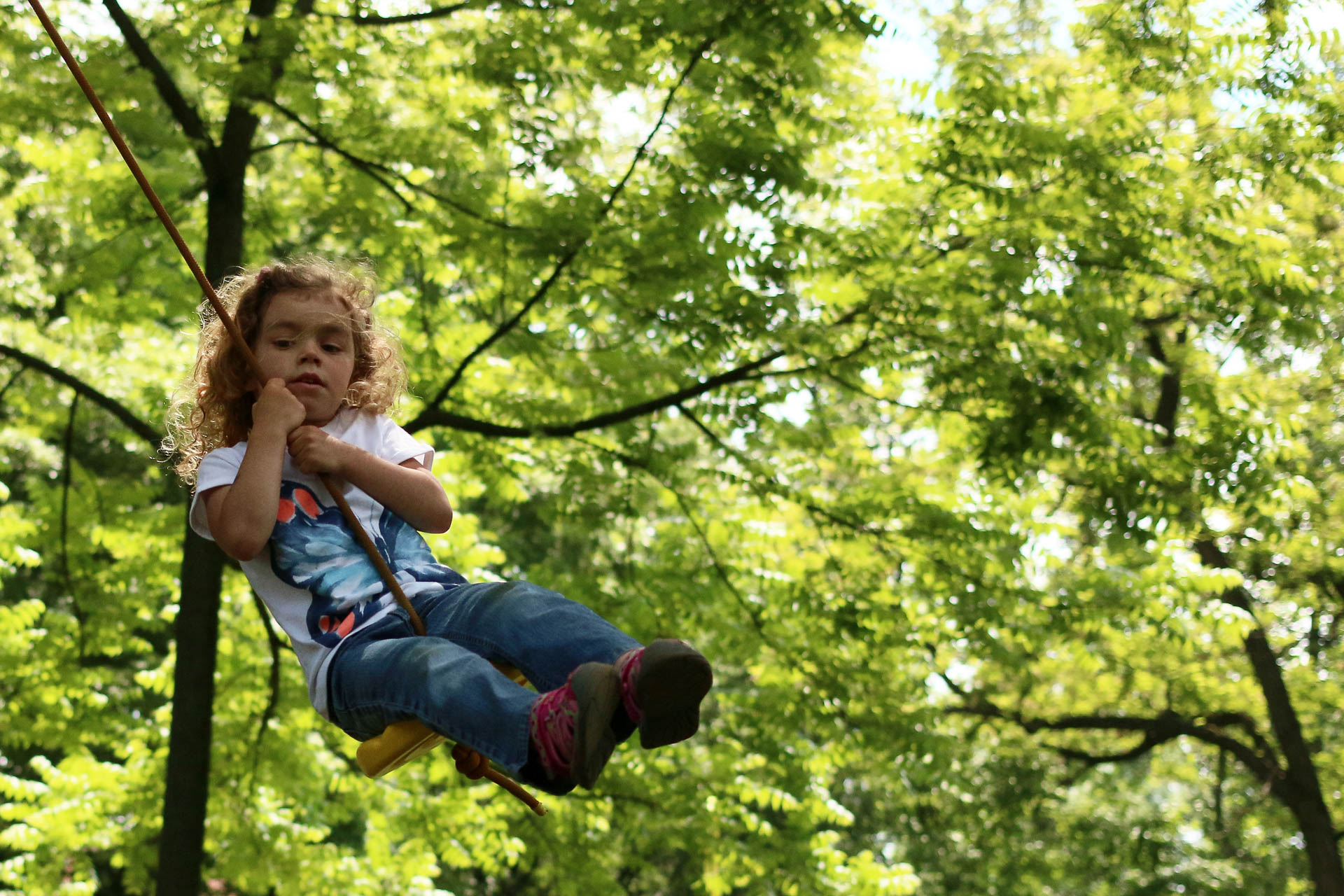 Malá holka na houpačce na pozadí stromů